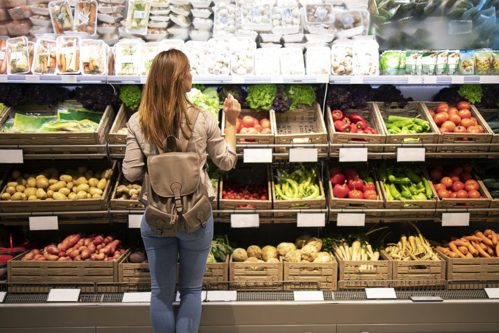 Good looking woman standing in front of vegetable shelves choosing what to buy. Copyright: @aleksandarlittlewolf/Freepik License.