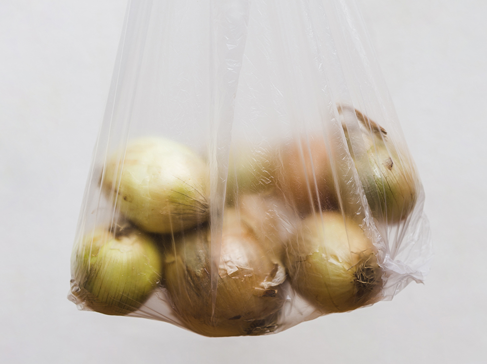 Harvest onions in transparent plastic bag on grey background. Copyright: Freepik.
