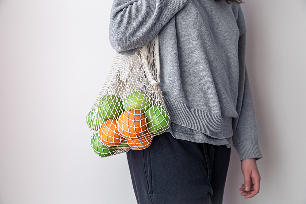 Close-up, a woman holds a string bag with apples and oranges.